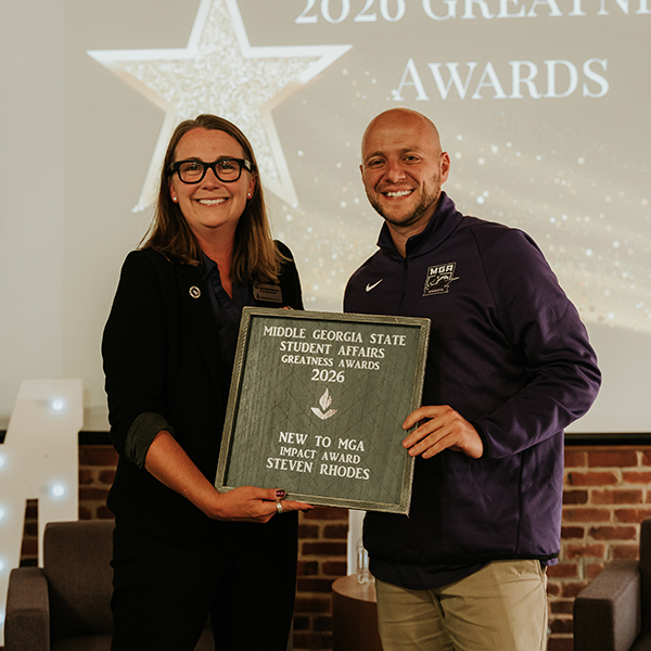 Dr. Jennifer Brannon and award recipient Stephen Rhodes smile while holding a plaque that reads, "Middle Georgia State Student Affairs Greatness Awards 2026 - New to MGA Impact Award, Steven Rhodes."